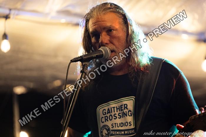 Bearded vocalist singing into a microphone while playing guitar.