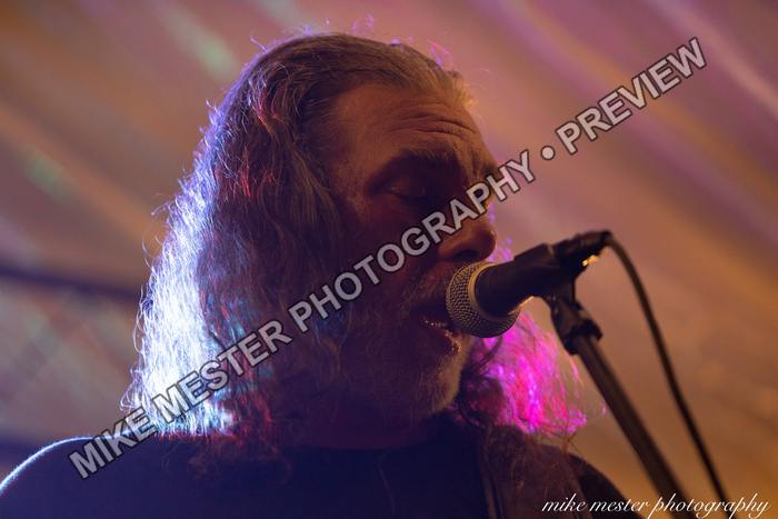 Bearded vocalist singing into a microphone under pink and blue light.