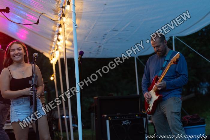 Female vocalist smiling beside a guitarist in a blue shirt.
