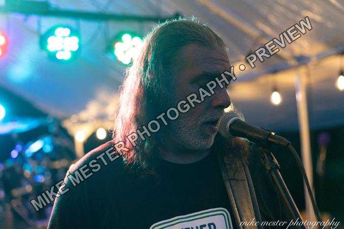 Long-haired vocalist singing in profile beneath blue stage light.