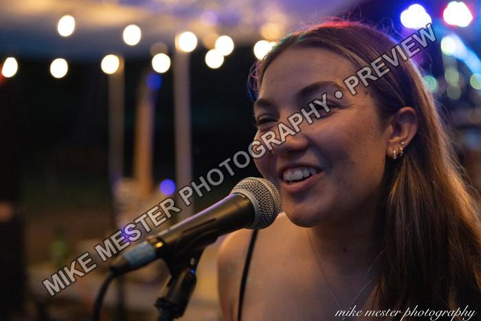 Female vocalist smiling during the performance beneath string lights.