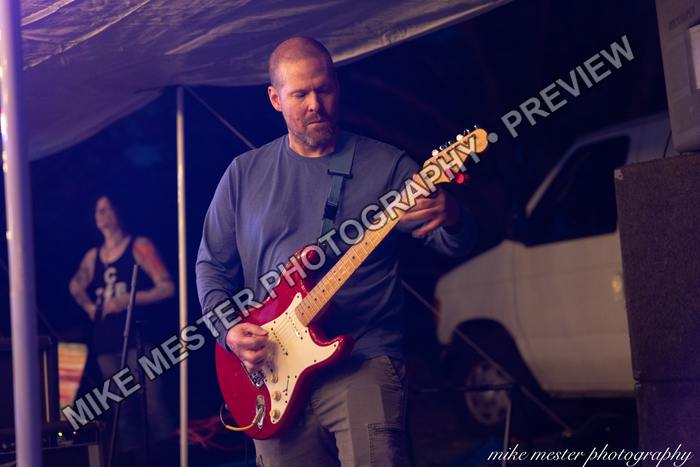 Guitarist playing a red electric guitar beside the stage.